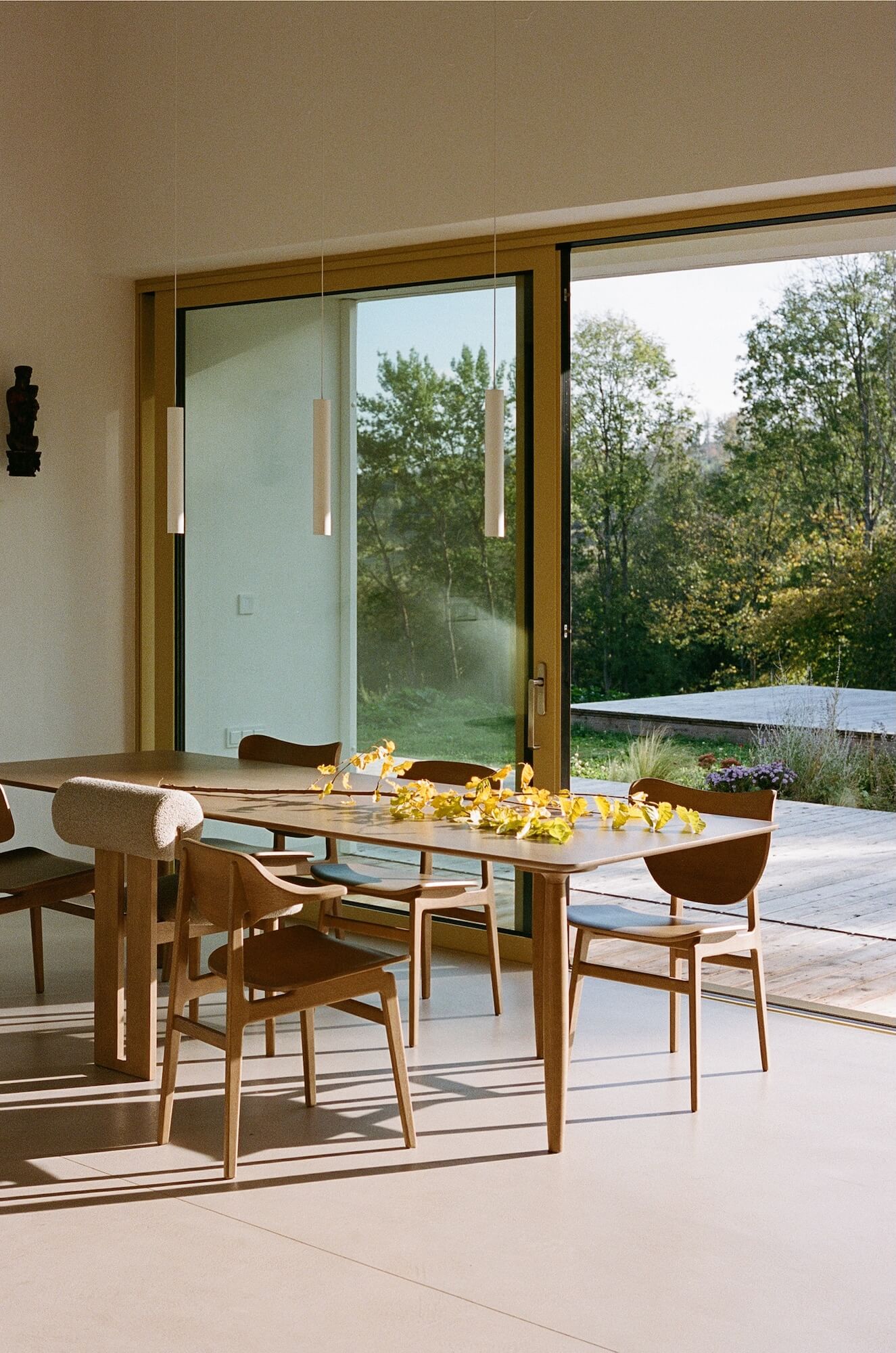 Modern dining area with wooden table and chairs near a large glass door with a view of trees.